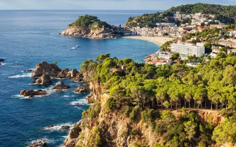 Scenic view of the Costa Brava coastline, a perfect stop on the way to Barcelona, with rugged cliffs, pine forests, and a charming town nestled by the sea.