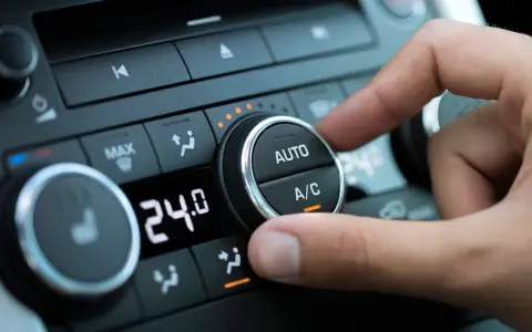 Dedo ajustando el dial del aire acondicionado del coche para comprobar el compresor. Se ve la pantalla digital con 24.0 grados.