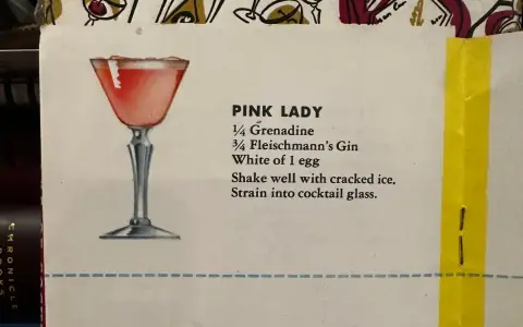 Elegancki kieliszek z różowym drinkiem Pink Lady, obok przepis na jego przygotowanie: grenadyna, gin i białko jaja.