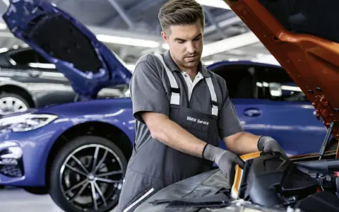 Mechaniker mit BMW Service Kleidung arbeitet an einem blauen BMW. Transparente Kosten für BMW Service.