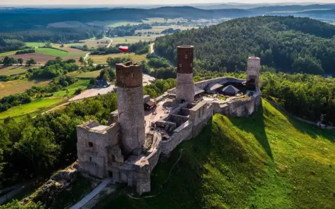 Zamek w Górach Świętokrzyskich, majestatycznie wznoszący się na wzgórzu, otoczony zielenią i malowniczym krajobrazem.