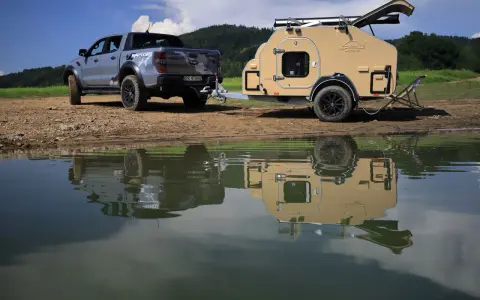 Srebrny Ford Raptor z przyczepą wyprawową Lifestyle Camper nad jeziorem.