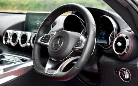 Interior de un coche deportivo Mercedes-AMG. Volante de cuero negro con controles, logo de Mercedes y detalles AMG.