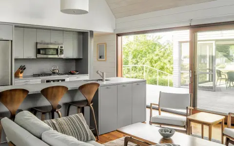 Cocinas abiertas al salón pequeñas con isla gris, taburetes de madera y vistas a un balcón verde.
