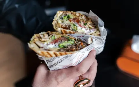 Pyszny kebab z Bukowiny Tatrzańskiej, pełen mięsa, warzyw i sosu, zawinięty w papier z gazetowym nadrukiem.