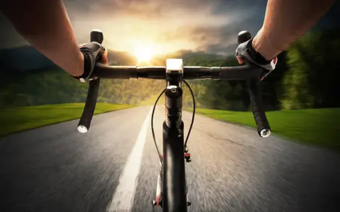 Rowerzysta w rękawiczkach pędzi po asfalcie. Słońce zachodzi, a krajobraz rozmywa się w tle. Ile czasu zajmie mu przejechanie 100 km rowerem?