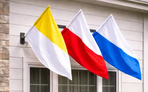 Trzy flagi: żółto-biała, czerwono-biała i niebiesko-biała, powiewają na wietrze. To może być flaga kościelna lub symbol parafii.
