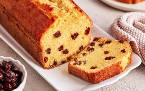 Ein saftiger Rosinenkuchen mit goldbrauner Kruste, auf einem weißen Teller angerichtet. Rosinen sind gut sichtbar im Teig verteilt.