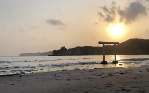Zachód słońca nad spokojnym morzem, z bramą torii na plaży w Japonii.