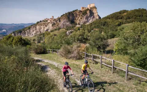 Ciclisti su una ciclabile panoramica con un borgo fortificato in lontananza, un'avventura tra le colline vicino a Rimini.