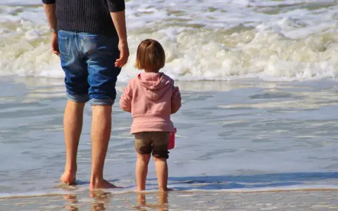Ojciec i dziecko na plaży, cieszący się wspólnym urlopem ojcowskim 9 tygodni.