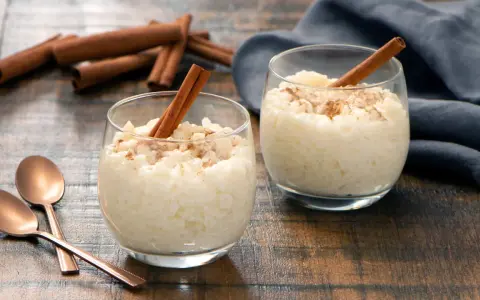 Dos copas de cremoso arroz con leche, espolvoreado con canela y decorado con una rama de canela.