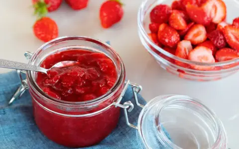 Słoik domowego dżemu truskawkowego, który zawiera pektynę, co to jest? Obok miska świeżych truskawek.