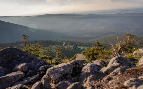 Widok z kamienistego szczytu na dolinę porośniętą lasem. W oddali widać zabudowania, być może schronisko sokolec, otoczone zielenią.