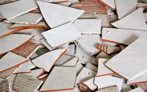 Stos białych, połamanych płytek ceramicznych z pomarańczowymi krawędziami. Wskazówka, jak zdjąć płytki ze ściany bez uszkodzenia.