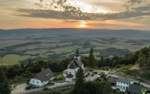 Zachód słońca nad iglicznym sanktuarium. Widok z lotu ptaka na kościół, budynki i krajobraz z pagórkami w oddali.