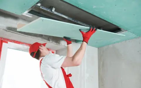 Handwerker mit roten Handschuhen montiert Gipskartonplatten an der Decke, um das Zimmer zu isolieren.