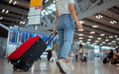 Kobieta z walizką na lotnisku, sprawdza swoją listę na wyjazd.
