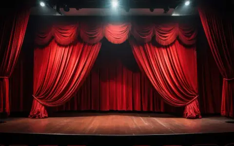 Czerwone, aksamitne zasłony w teatrze, gotowe do odsłonięcia sceny. Podłoga lśni, a światła z góry oświetlają pustą przestrzeń, czekającą na spektakl.