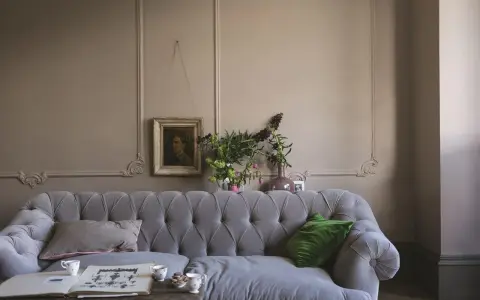 Szara kanapa w salonie z obrazem i bukietem kwiatów. Dominują **kolory ziemi**, tworząc przytulną atmosferę.
