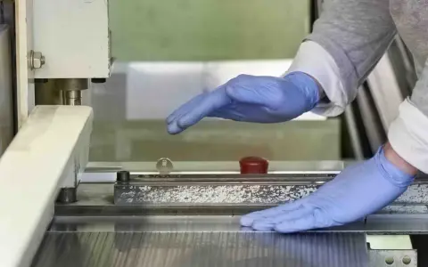 Manos enguantadas operan una máquina que parece ser una cizalla, lista para cortar material.