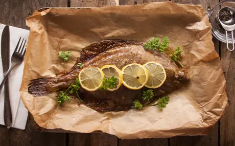 Gebackene Scholle mit Zitronenscheiben und Petersilie auf Backpapier. Perfekt zum Scholle essen!