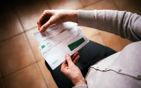 Dłonie trzymają kopertę ZUS. W środku decyzja o waloryzacji emerytury, być może zapowiedź trzynastej emerytury.