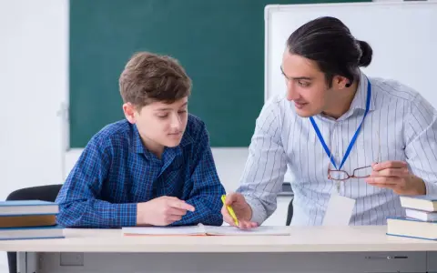Nauczyciel wyjaśnia uczniowi rzeczownik pytania i przykłady, wskazując na zeszyt.