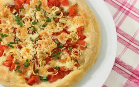 Pizza casera con tomates, queso derretido, cebolla y cebollino. Los ingredientes de esta pizza casera lucen deliciosos.