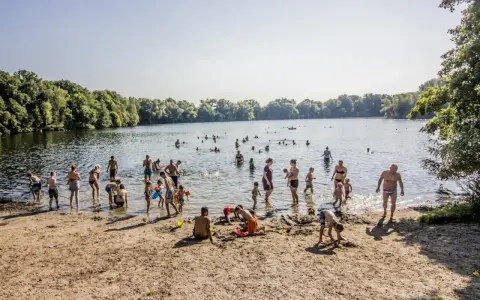Menschen genießen einen sonnigen Tag im Strandbad Hamburg. Kinder spielen im Sand, während Erwachsene im Wasser planschen.