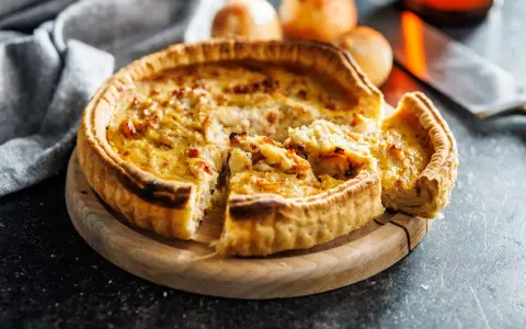 Une part de quiche lorraine, une des spécialités lorraines, sur une planche en bois.