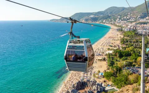 Seilbahn über dem belebten Alanya Strand mit türkisfarbenem Meer und vielen Sonnenanbetern.