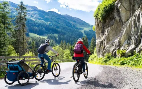 Zwei Radfahrer mit Rucksäcken und Anhänger fahren auf einer Bergstraße.