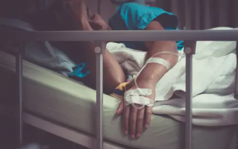 Pacjent w łóżku szpitalnym, z kroplówką, cierpiący. Może to być objaw wstrząsu septycznego, kod ICD-10 A41.