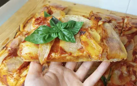 Una fetta di pizza di patate dorata, guarnita con basilico fresco, pronta per essere gustata.