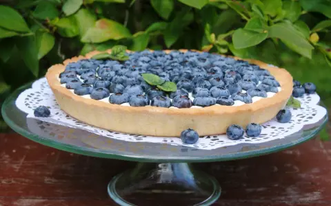 Pyszna tarta z borówkami, udekorowana listkami mięty, prezentuje się apetycznie na szklanej paterze.