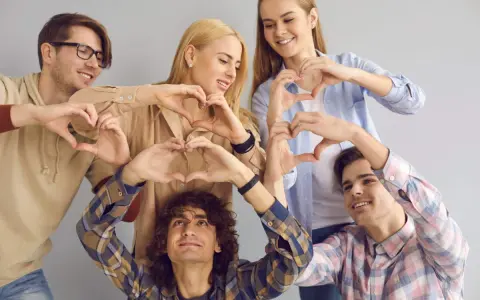 Cinco jóvenes sonríen formando corazones con sus manos, un gesto que puede servir como frases enseñar sobre la amistad y el amor.