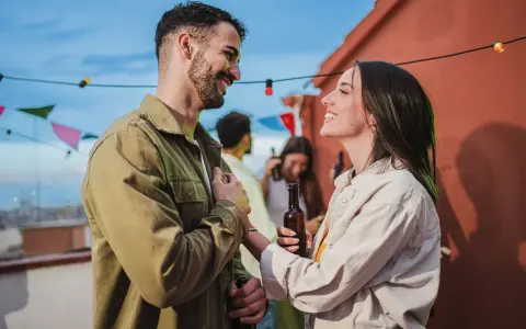 Uśmiechnięty mężczyzna, który zabiega o kobietę, trzyma butelkę piwa na imprezie na dachu.
