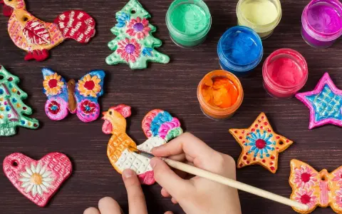 Dziecko maluje koguta z masy solnej. Wokół kolorowe ozdoby i farby, idealne do tworzenia własnych dekoracji masa solna diy.