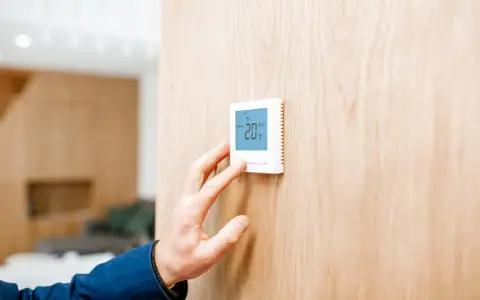 Mano ajustando un termostato digital, parte de los sistemas de calefacción, mostrando 20°C en una pared de madera.