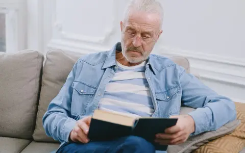 Starszy mężczyzna w okularach czyta książkę, szukając sposobów, jak poprawić pamięć.