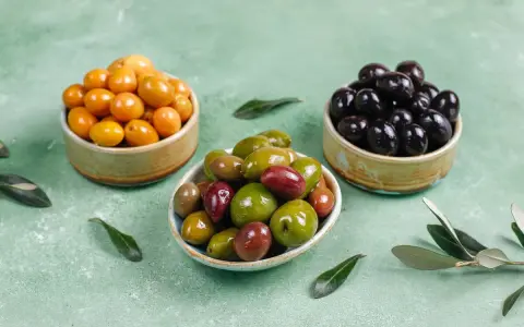 Tres cuencos con aceitunas de diferentes colores: amarillas, verdes y negras.