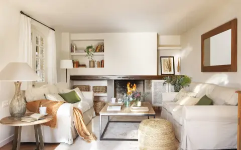 Salón acogedor con chimenea encendida, sofás blancos, mesa de centro de madera y detalles decorativos.
