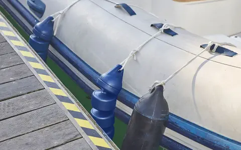 Un bateau pneumatique est amarré à un quai, avec des pare-battages bleus et noirs prêts à gonfler pour protéger la coque.