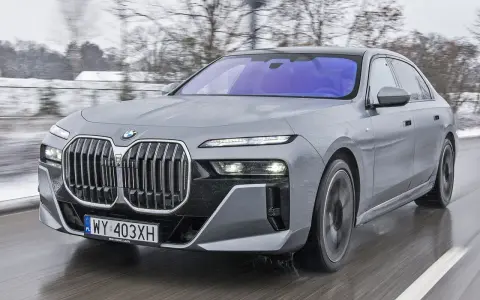 Szary BMW M7 pędzi po mokrej drodze, otoczony zimowym krajobrazem.