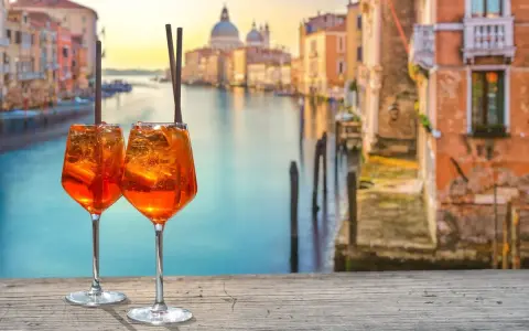 Zwei Aperol Spritz auf einem Holztisch mit Blick auf den Canal Grande in Venedig. Perfekt für einen Aperitif in der spritz bar.