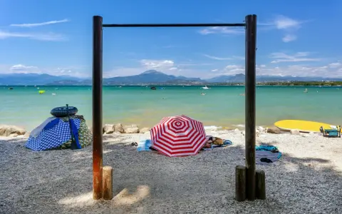 Słoneczne plaże nad Jeziorem Garda, z turkusową wodą, górami w tle i kolorowymi parasolami.