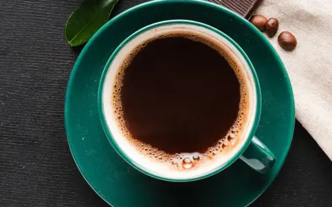 Aromatic coffee in a green cup, next to chocolate and beans. Czy kawa podnosi kortyzol? This morning brew might be the answer.