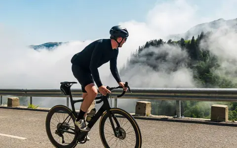 A cyclist in black gear conquers a mountain road, enjoying the breathtaking views and the freedom of long rides amidst swirling clouds.