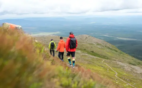 Tre vänner på vemdalen vandring njuter av den vidsträckta utsikten över skogar och berg under en molnig himmel.